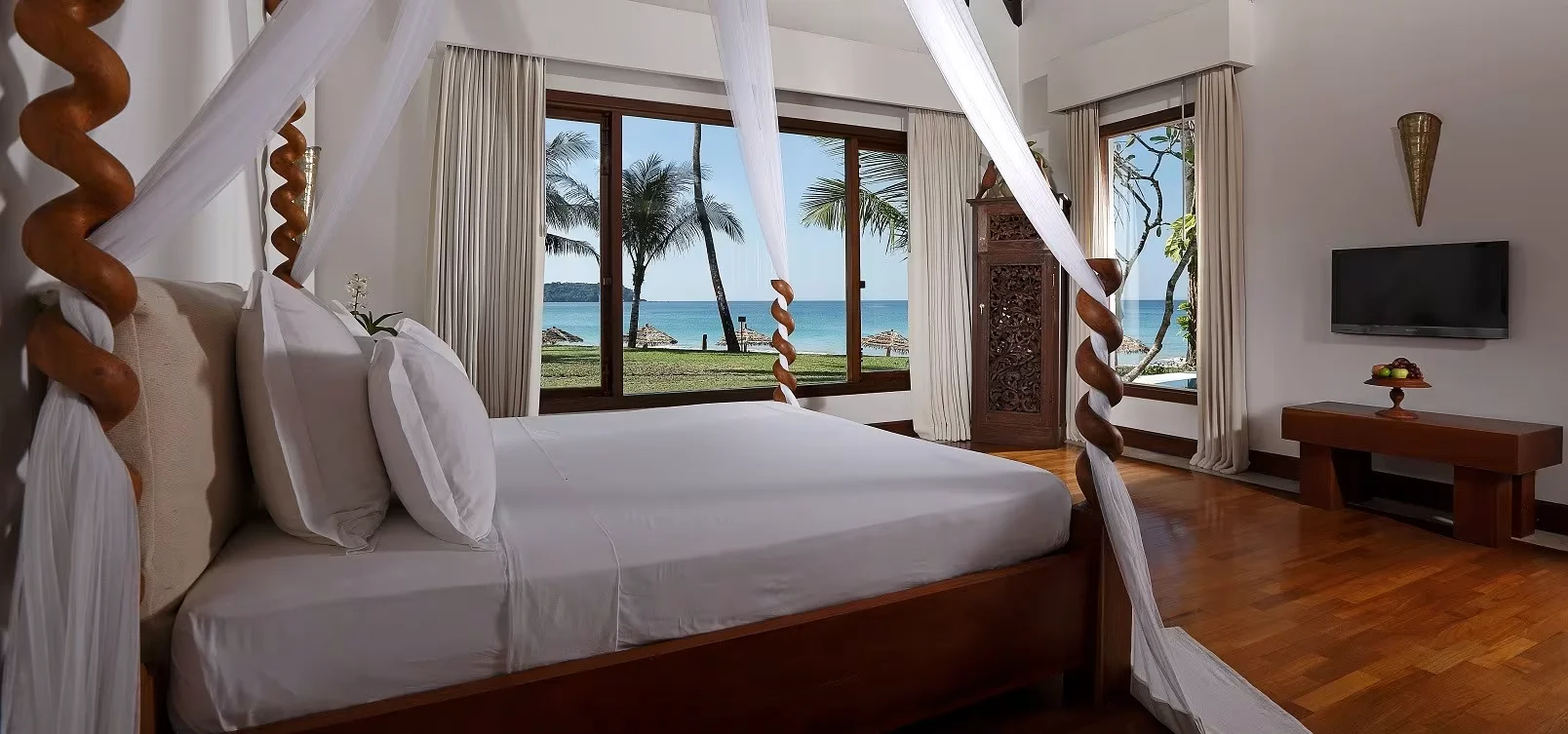 A seaside guest room with a carved four-poster hardwood bed and an ocean view