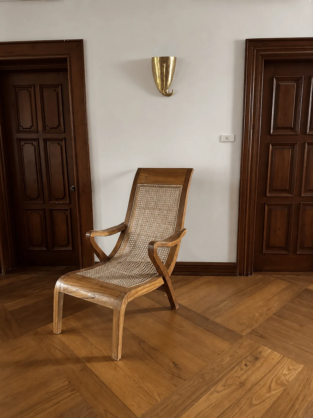 A handmade hardwood lounge chair with a woven cane seat between panelled timber doors