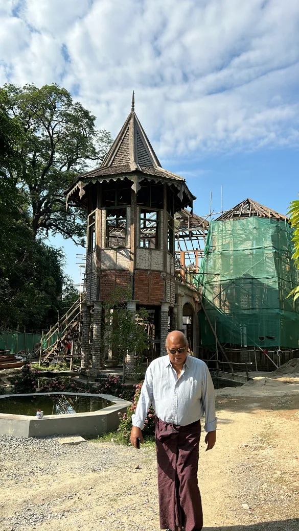 Double-click to enlarge U Kyaw Sein walking on site in front of a restoration under scaffolding